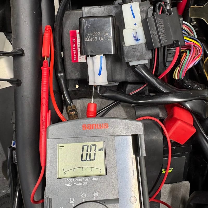 ECUの横に付いたウインカーリレー。白い2極カプラーの裏からテスターの針を刺し、キーOFFでsanwaのテスターが0.0mVを表示している