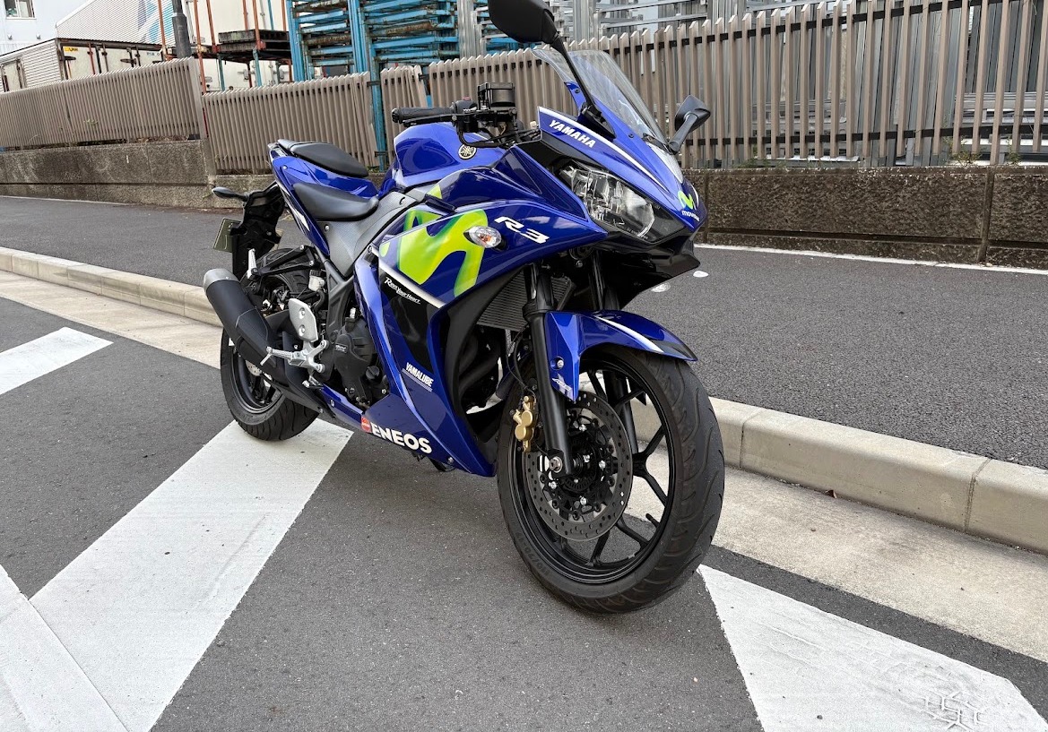 停車中のYAMAHA YZF-R3（Movistarカラー）を右斜め前から。背景はフェンスと建物