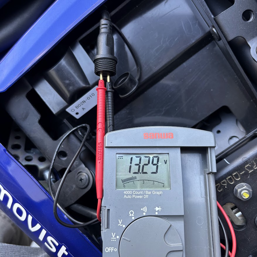 YZF-R3のバッテリー充電用車両側ケーブル（オカダ電機 ACH-22）にテスターの赤黒プローブを挿し込み、電圧13.29Vを計測している