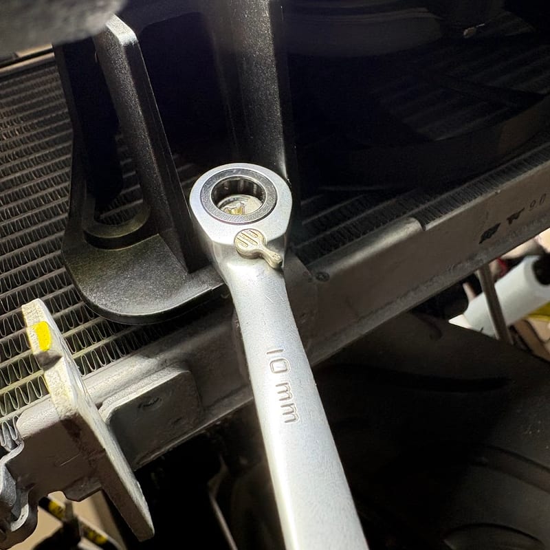 ラジエター裏のファンの下側のボルトに、10mm のギアレンチを掛けているところ