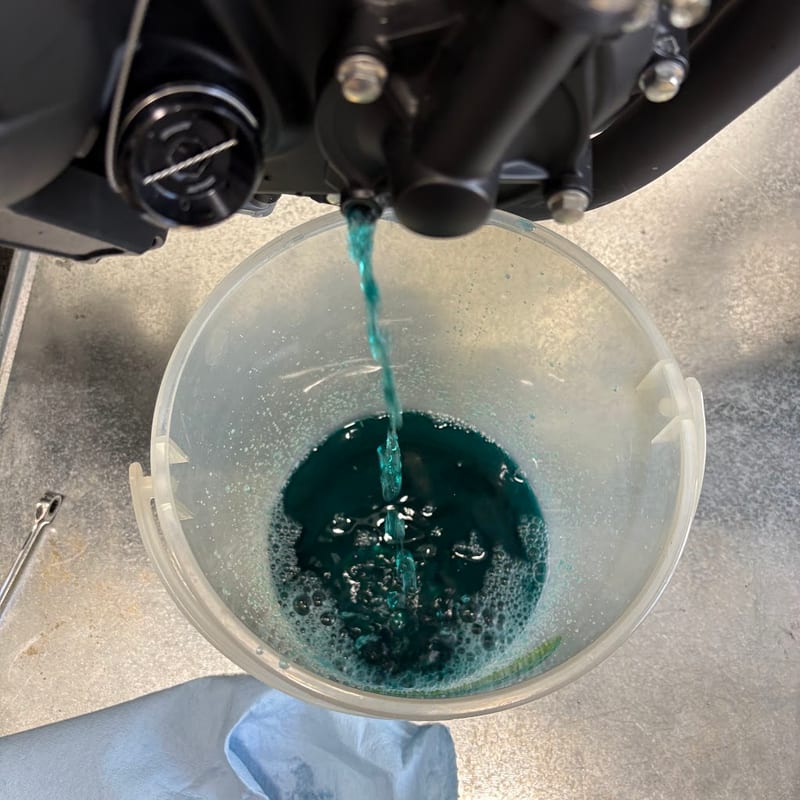 ドレンボルトの穴から受け皿へ流れ落ちる緑色の冷却水