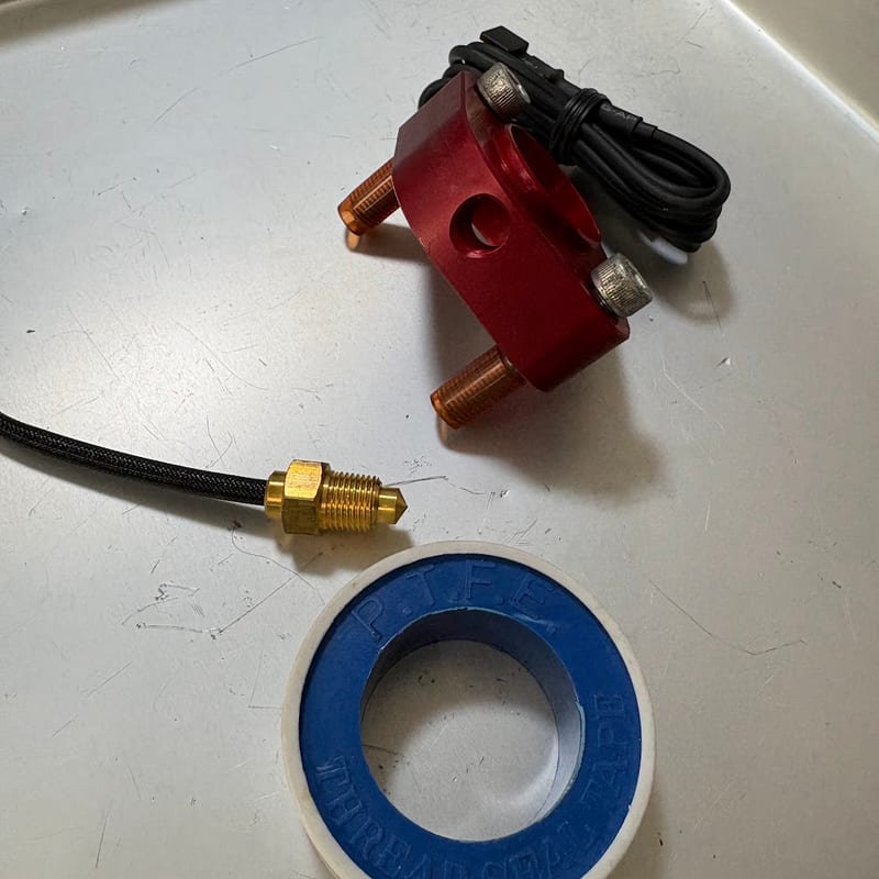 サーモスタットキャンセルに通した付属の長いボルト2本と、KOSO の水温センサー、シールテープ