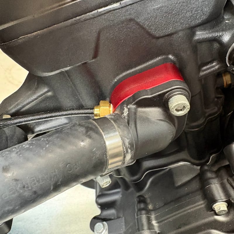 エンジンとサーモスタットカバーのあいだの赤いキャンセル。側面に真鍮の水温センサーが入り、黒い編組の線が出ている