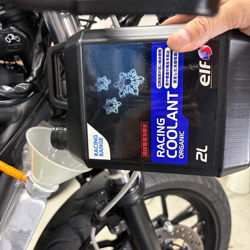 フィラーネックに差したじょうごへ、elf RACING COOLANT ORGANIC の2L缶から注いでいるところ