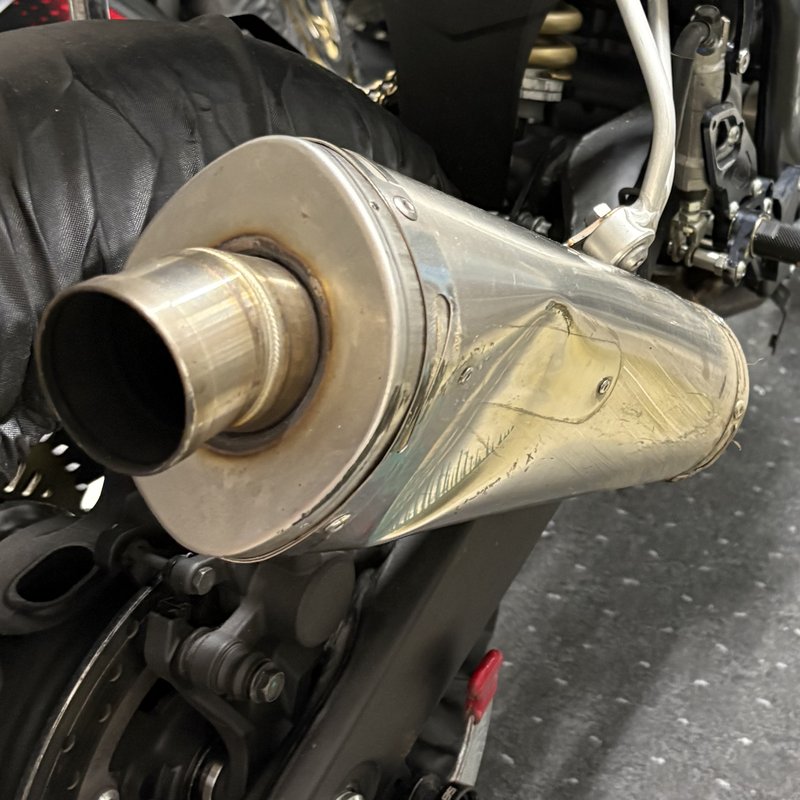 転倒後の YZF-R25 のサイレンサー。本体に折れたような筋があり、カーボンのエンドキャップが無く、内側のパイプが見えている