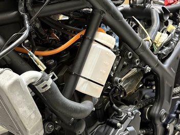 フレームに留めた半透明のキャッチタンクと、エンジンの上を通るオレンジのシリコンホース
