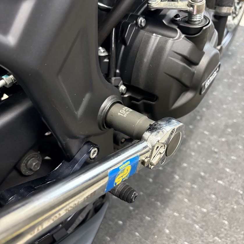 車体右側から、19mmのディープソケットを付けたトルクレンチでピボットシャフトナットを締めているところ