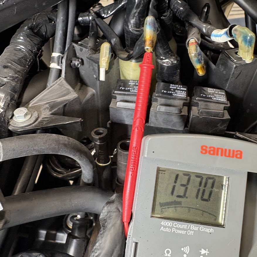 左コイル側の配線にテスターの赤いプローブを当て、サンワのデジタルテスターが13.70Vを表示している