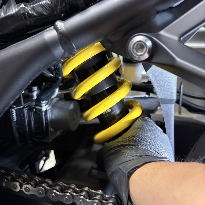 ボルトを抜いた純正リアショックアブソーバーを手で引き出しているところ。ダンパーボディにKYBの刻印がある