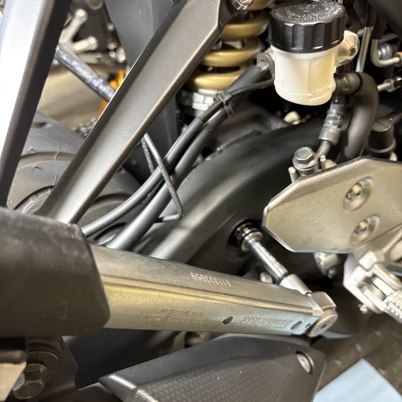車体右側から、エクステンションバーを継いだトルクレンチでリヤショックアブソーバーAss'yボルト（下側）を締めているところ