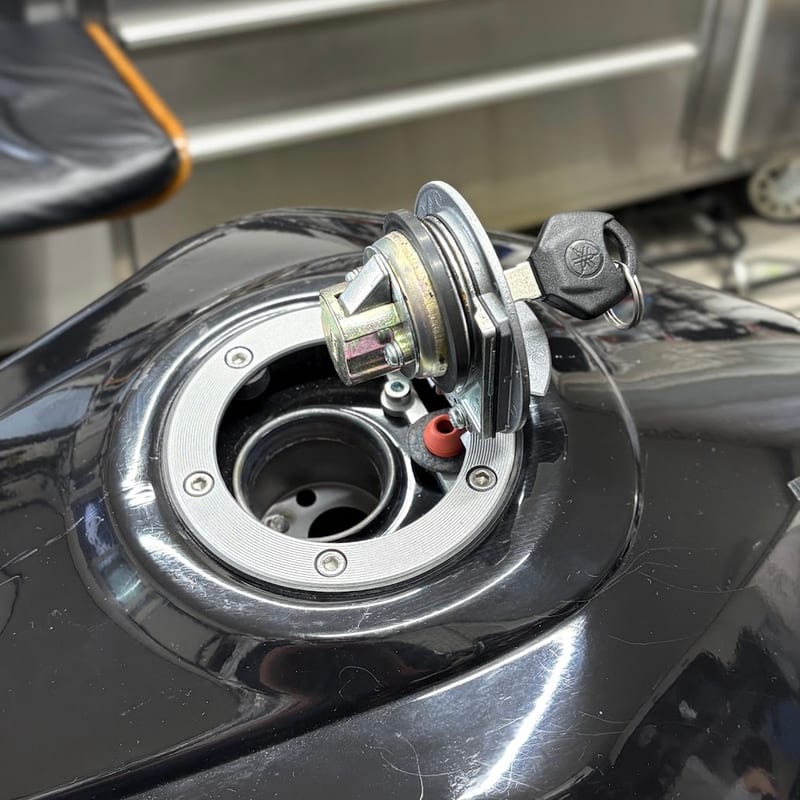 キーを差したまま開けた純正タンクキャップ。キャップの裏のロック機構と給油口が見える