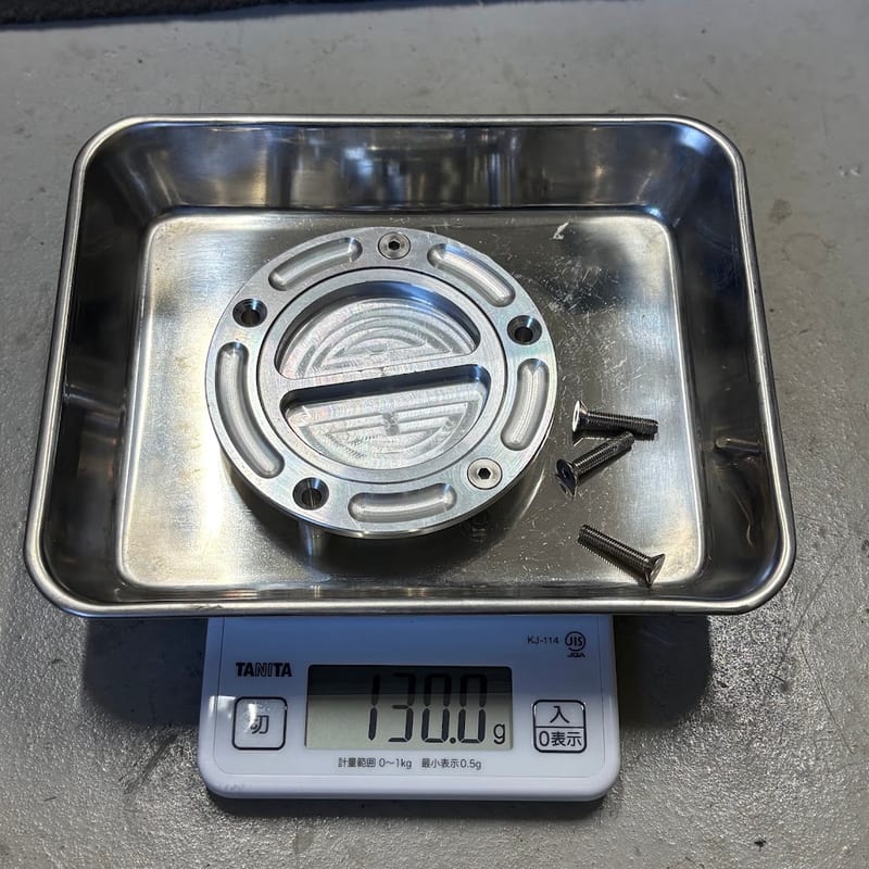 はかりに載せたアルミ製タンクキャップとボルト3本。表示は130.0g