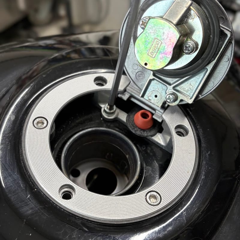 キーで開けた純正タンクキャップの、内側の短いボルトに六角レンチを差し込んでいる