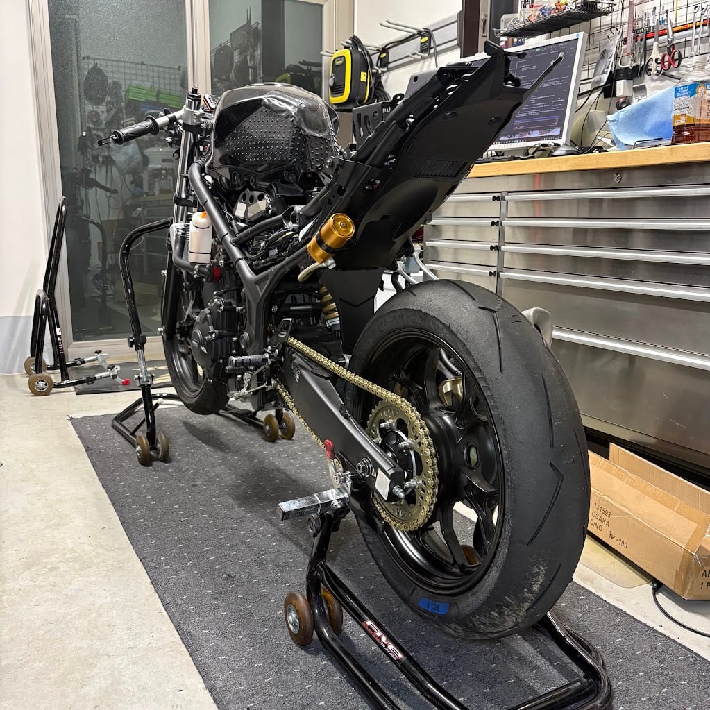 タイヤ交換後のYZF-R3の左後方。リアスタンドで上げた後輪に、SC1の青いシールが貼られたスーパーコルサ V4が付いている