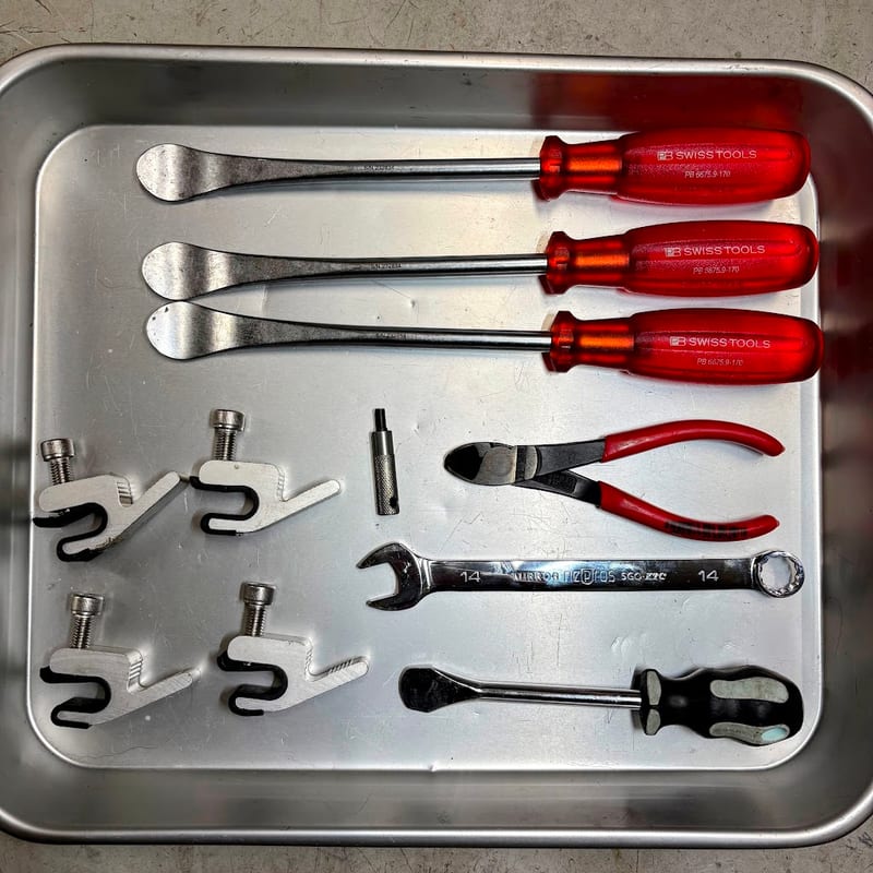 トレーに並べた工具。PB SWISS TOOLSのタイヤレバー3本、デイトナのビードダウンキーパー4個、DRCのバルブコアドライバー、KNIPEXのニッパー、KTCネプロスの14mmコンビネーションレンチ、コインドライバー
