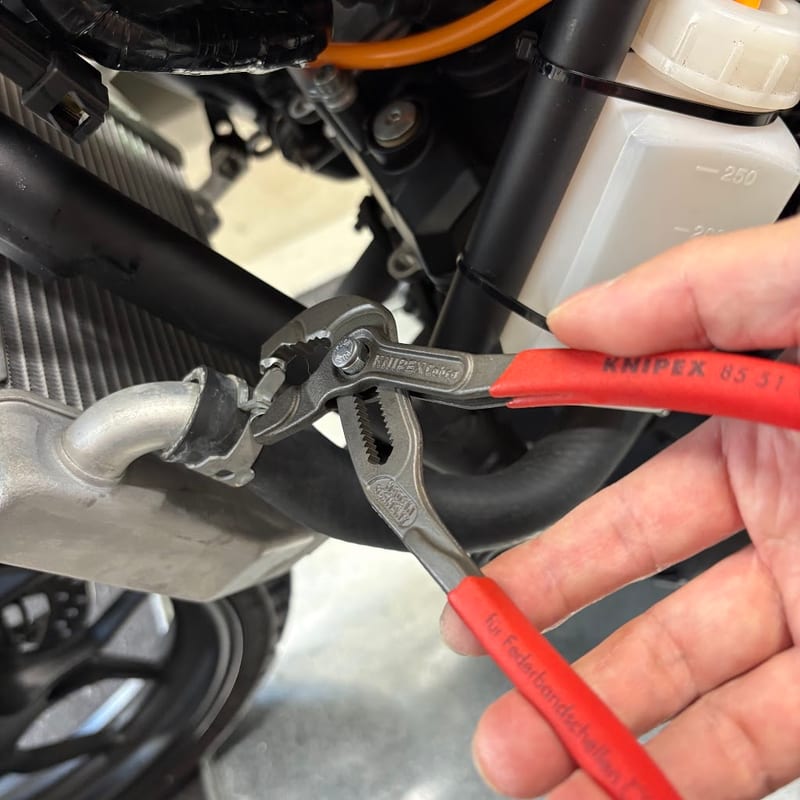 ラジエターのパイプに差したホースのばね式のクリップを、KNIPEX のホースクリップ用プライヤーで挟んでいるところ