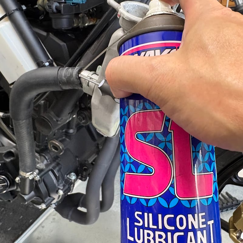 ホースとパイプのすき間に、ワコーズのシリコンスプレーのノズルを当てて吹いているところ