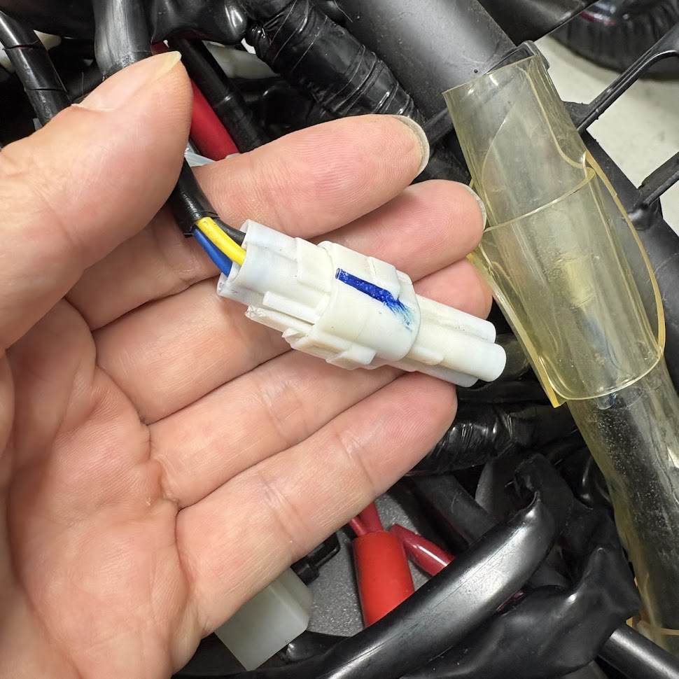 車体側のハーネスにあるテールライトの白い3極防水カプラーを手のひらに載せたところ。黄色と青の線が出ている
